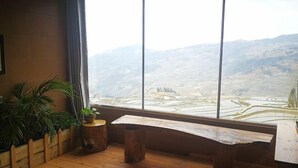 Een kamer met een groot raam, houten vloer, een bankje en potplanten.