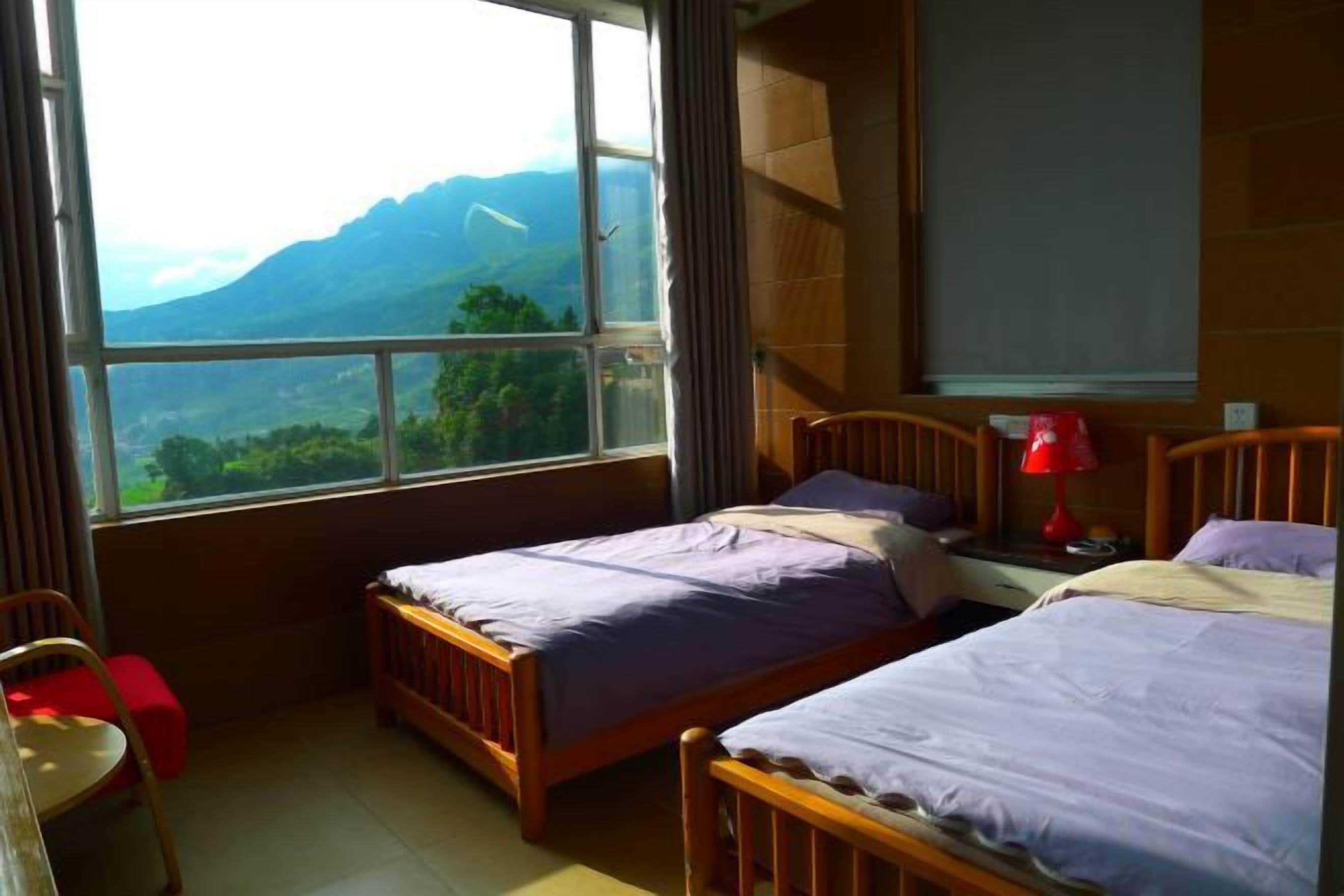 A bedroom with two beds, a window with a mountain view, a desk, and a chair.