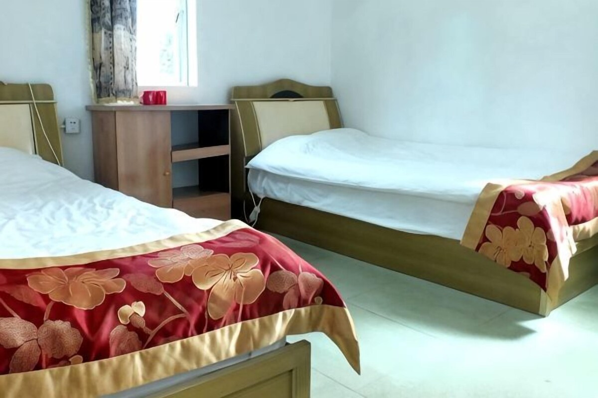Una habitación con dos camas individuales, un escritorio pequeño y una ventana con cortinas.