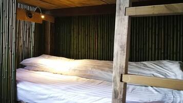 Una cama litera con ropa blanca en una habitación con paredes de bambú y techo de madera.