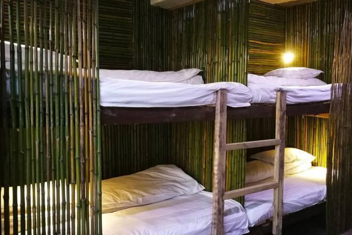 Ein Stockbett mit weißer Bettwäsche, einer Holzleiter und Bambuswänden.