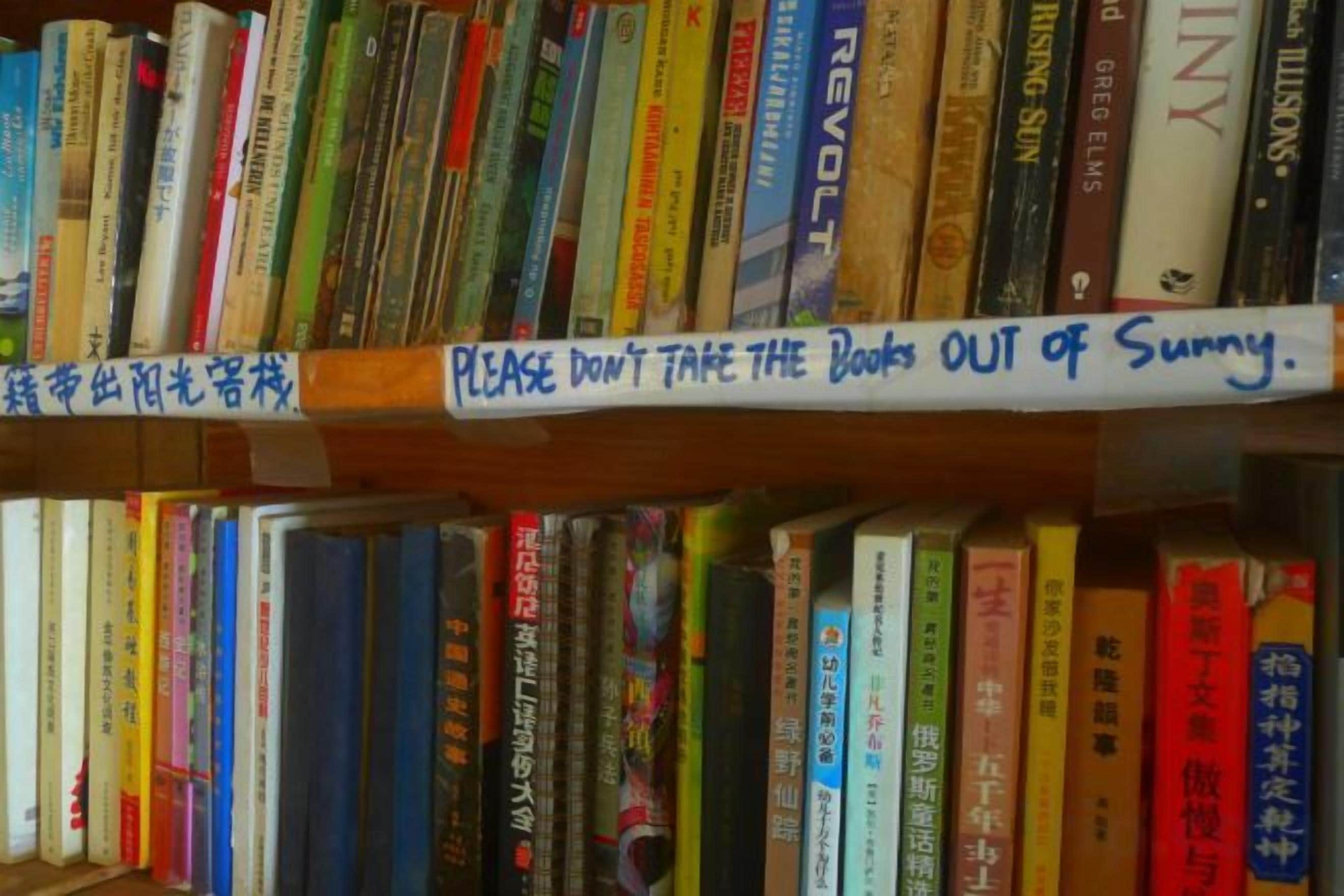 A bookshelf with a sign that reads 'PLEASE DON'T TAKE THE BOOKS OUT of Sunny.'