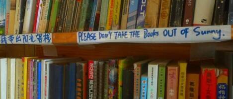A bookshelf with a sign that reads 'PLEASE DON'T TAKE THE BOOKS OUT of Sunny.'