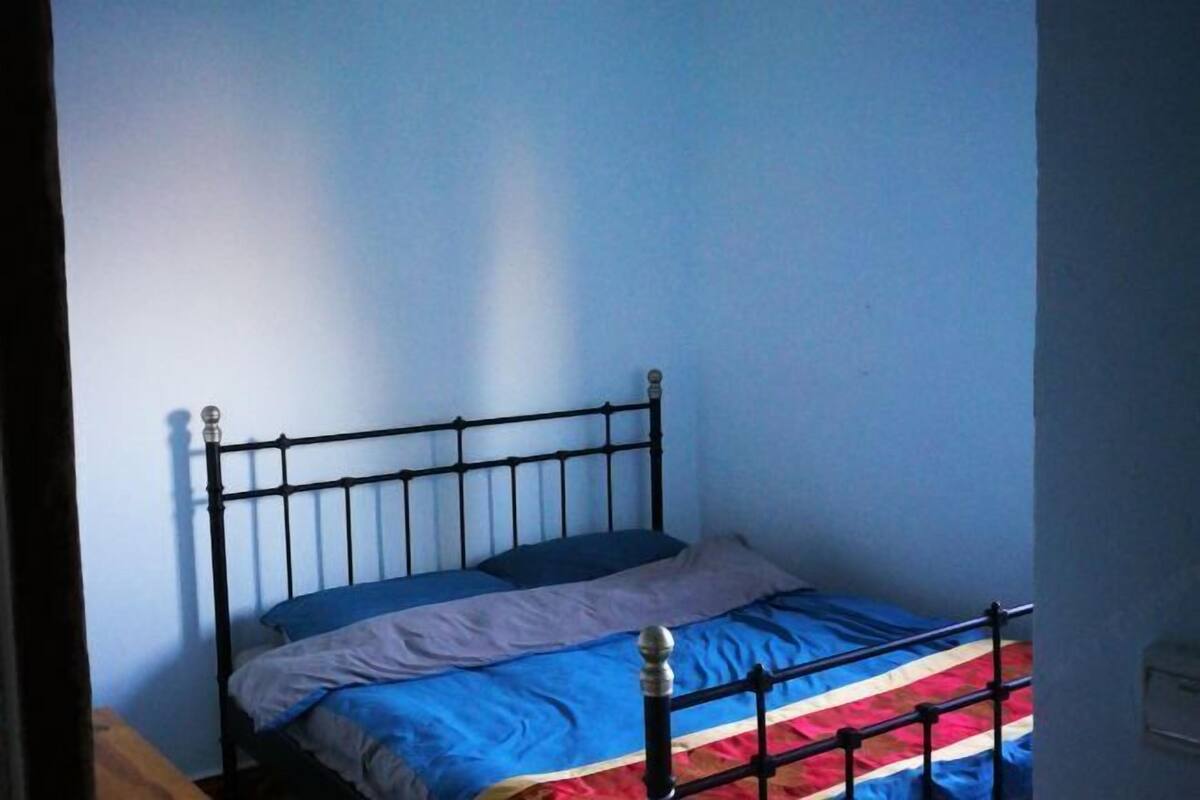 Ein Einzelbett mit Metallgestell, eine blaue Wand und ein kleiner Holztisch.
