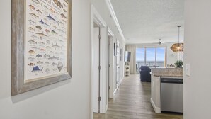 En hall med en inramad illustration av en fisk på väggen, som leder vidare till ett köksområde med utsikt över havet.