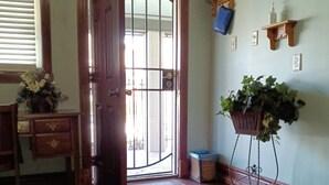 A wooden door with a glass panel, a wooden bench, a potted plant, a rug, and a wall-mounted shelf with a flower picture.