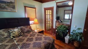 A bedroom with a bed, a nightstand, a lamp, a mirror, and a door.