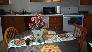 Une cuisine avec des meubles de rangement en bois, un four à micro-ondes, une cuisinière et un évier. On y trouve une table recouverte d’une nappe et un vase rempli de fleurs.