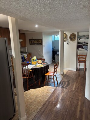 A dining area with a table set for four, a refrigerator, and a kitchen in the background.