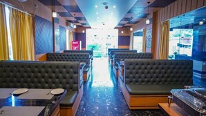 Un restaurant avec une allée centrale, des banquettes noires rembourrées et une table en verre avec des assiettes.