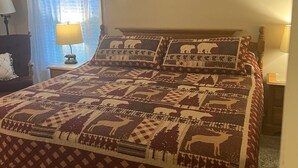 Un dormitorio con una cama grande, una ventana con cortinas, un panel decorativo con un paisaje forestal en la pared y dos lámparas de noche.