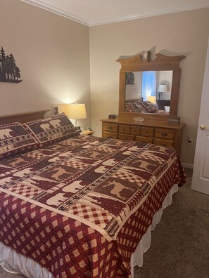 Ein Schlafzimmer mit einem großen Bett, einer Holzkommode, einem Spiegel und einem Nachttisch mit Lampe.