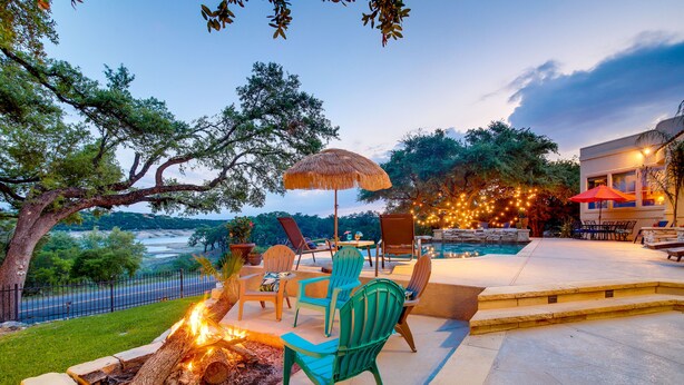 An outdoor patio with a fire pit, chairs, and an umbrella. - Luxe Lake Travis Vacation Rental w/ Heated Pool (Lago Vista)