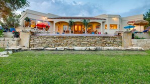 A modern house with a stone facade, a patio with lounge chairs, and a stone wall in the foreground. - Luxe Lake Travis Vacation Rental w/ Heated Pool (Lago Vista)