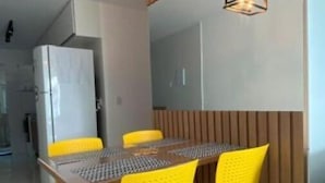 Ruokailutilassa on puinen pöytä ja keltaiset tuolit, jääkaappi sekä riippuvalaisimet.