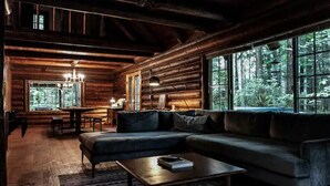 A log cabin interior with a large sofa, a coffee table, and a dining area.
