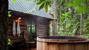 A rustic cabin with a wooden hot tub, a bench, and a covered seating area.