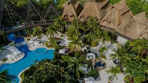 Un resort con una amplia piscina, palmeras y construcciones de techo de paja.