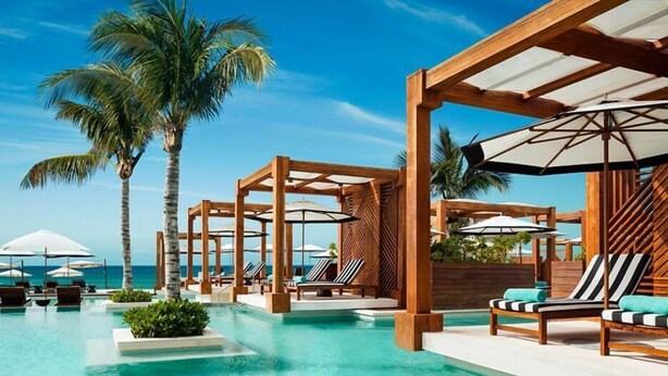 Zona de piscina en un resort con pérgolas de madera, sillas de descanso y sombrillas.