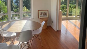 A spacious dining area with a round table and white chairs, large windows offering a view of greenery and houses, and a chandelier hanging from the ceiling. - Stylish CBD apartment with stunning river views (Hamilton)