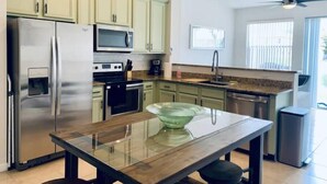 Une cuisine moderne dotée d’appareils électroménagers en acier inoxydable, d’une table à manger au plateau en verre et de meubles de rangement vert clair.