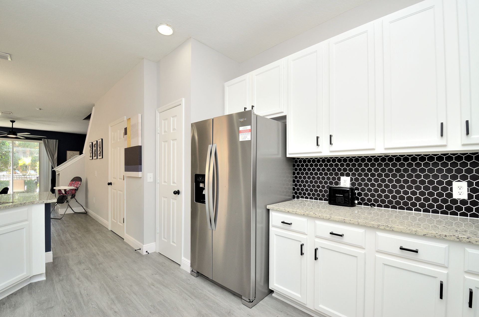 A modern kitchen with white cabinetry, a stainless steel refrigerator, and a hexagonal tile backsplash.