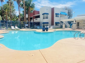 A swimming pool with lounge chairs, a building with a number 11, and palm trees.