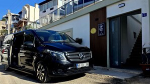Un Mercedes-Benz negro estacionado frente a un edificio moderno con un cartel que indica 'ILYA APARTS NO:15'.