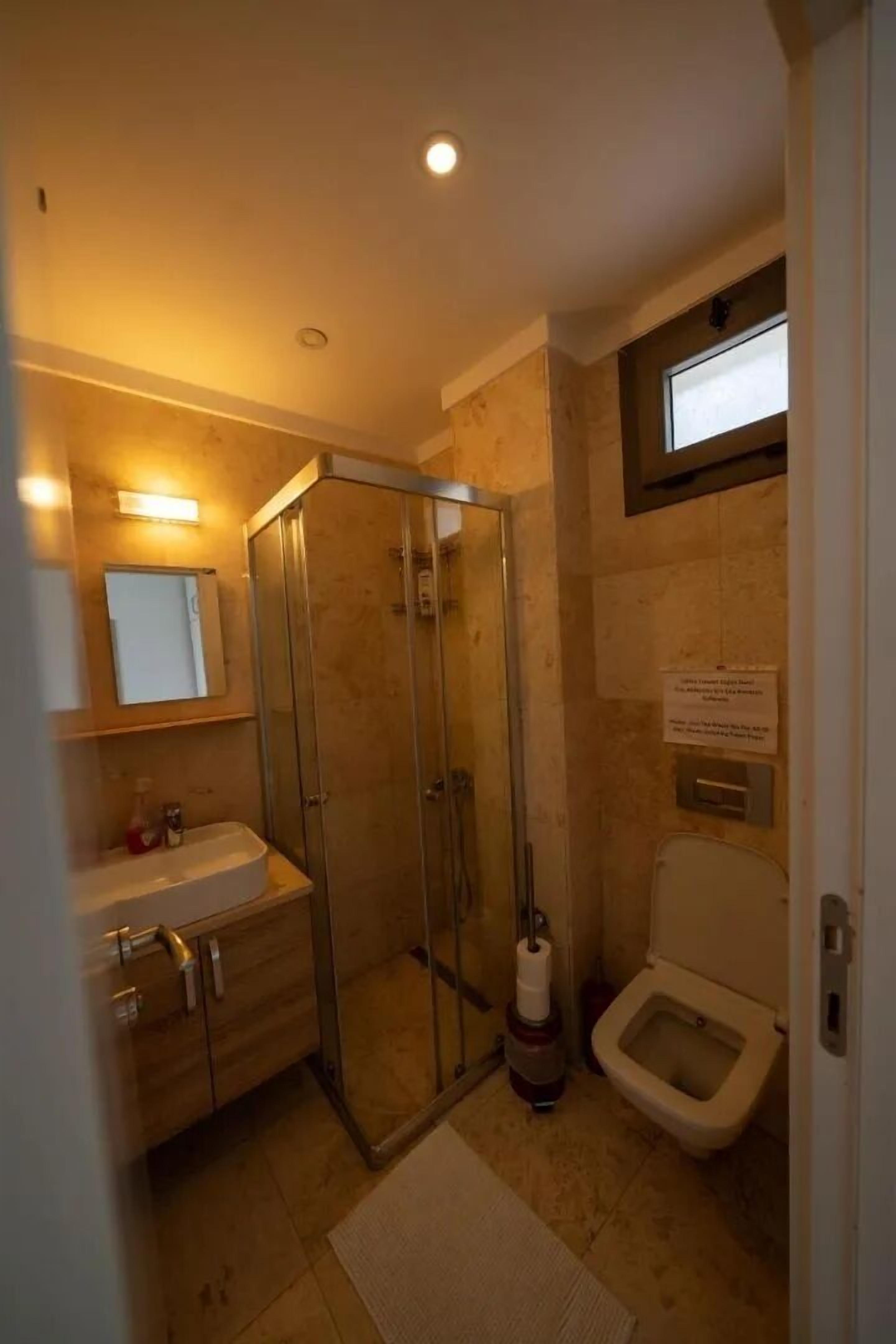 Ein kleines Badezimmer mit Duschkabine aus Glas, Toilette und Waschbecken mit Spiegel darüber.