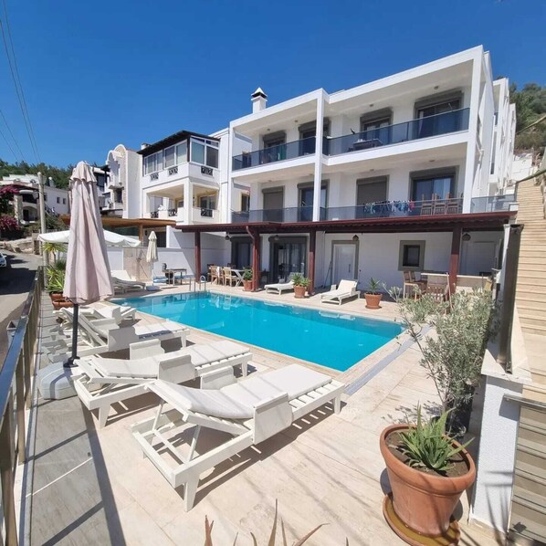 A modern two-story building with a swimming pool, sun loungers, and potted plants. - İlya Apart 1. (Bodrum)