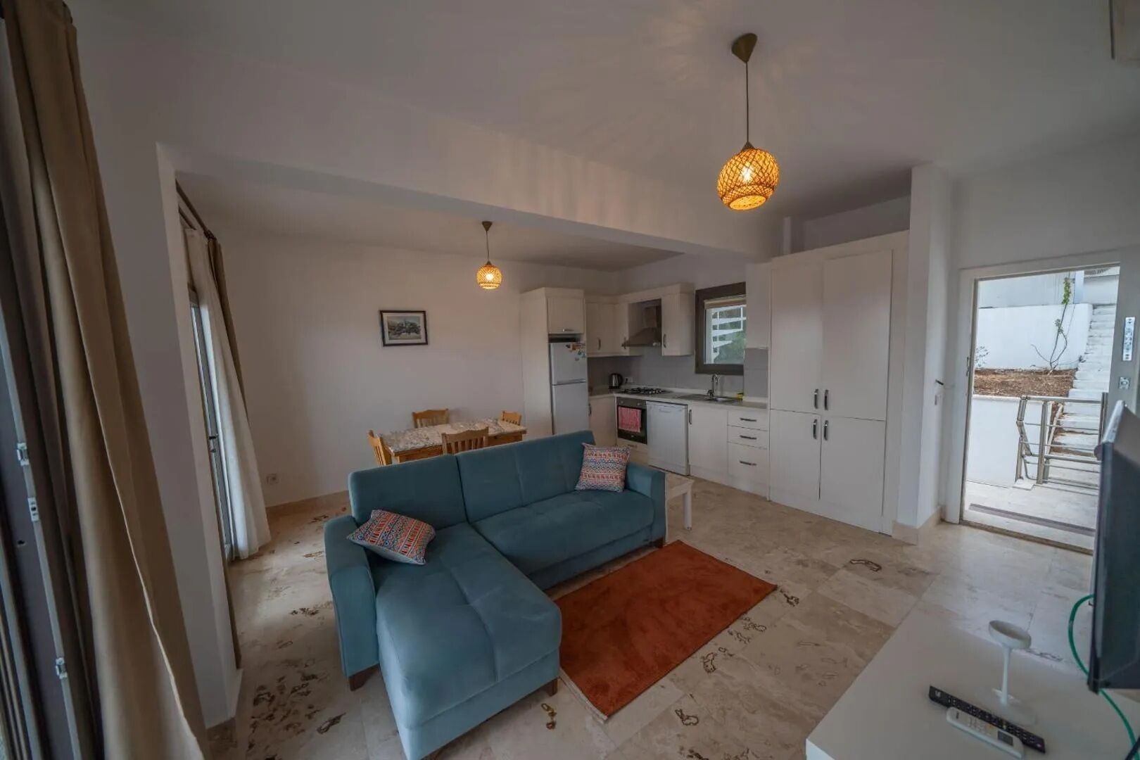 A modern apartment with a blue sofa, a dining table, a kitchen, and a balcony.