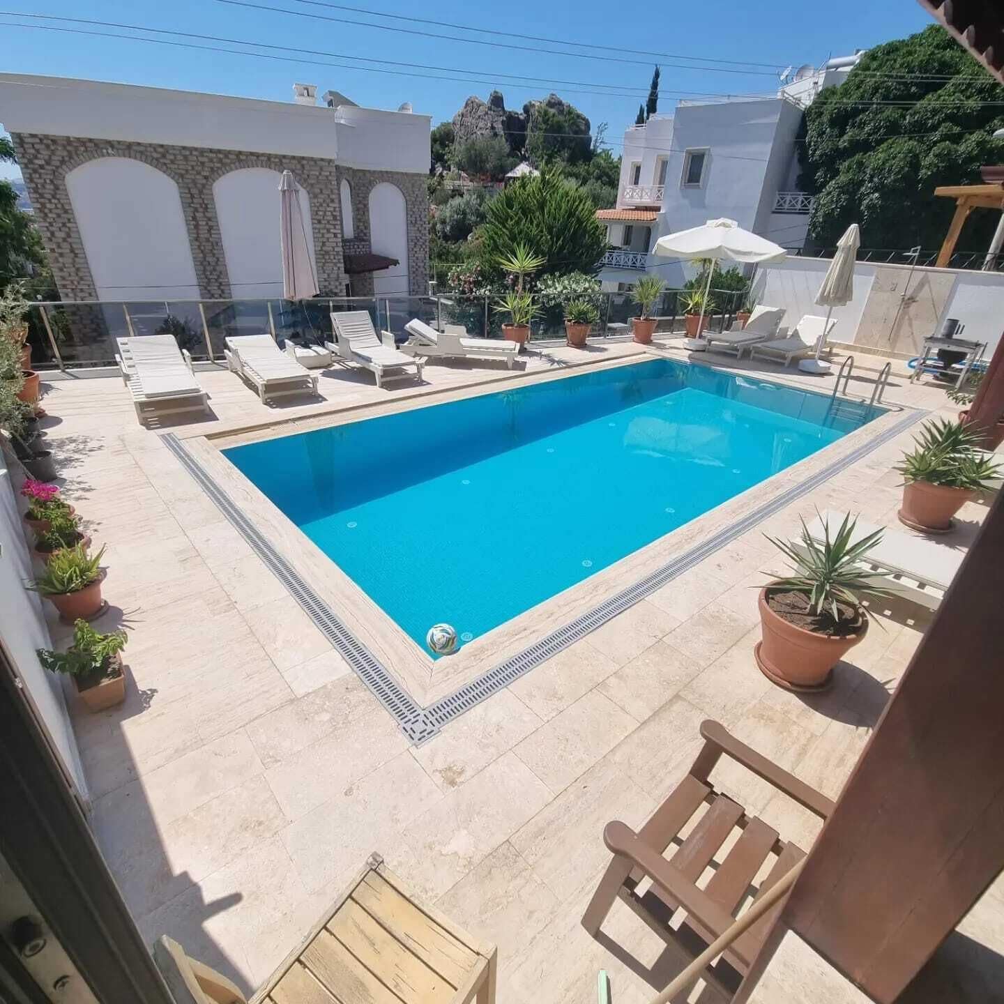 Une piscine rectangulaire entourée de chaises longues et de plantes en pot.