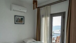 Habitación de hotel con dos camas, un cuadro en la pared, aire acondicionado y vista al mar a través de una puerta.