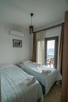 Habitación de hotel con dos camas, un cuadro en la pared, aire acondicionado y vista al mar a través de una puerta.