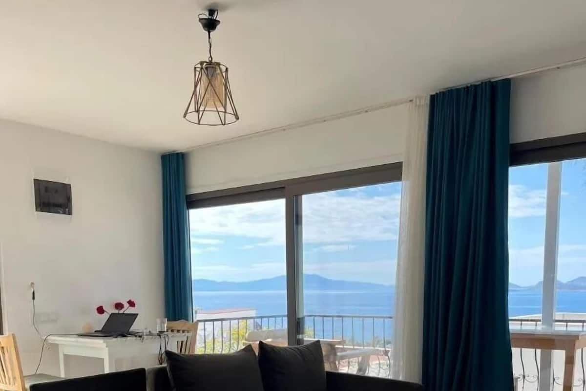 A modern living room with a sectional sofa, a small white table, and a balcony with a view of the sea.