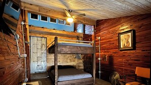 A bunk bed room with wooden walls, a ceiling fan, a framed picture on the wall, and a chair. - Amazing repurposed grain elevator! (Sabin)