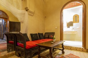 A traditional room with a sofa set, a wooden table, and a view of a bathroom through an arched doorway.