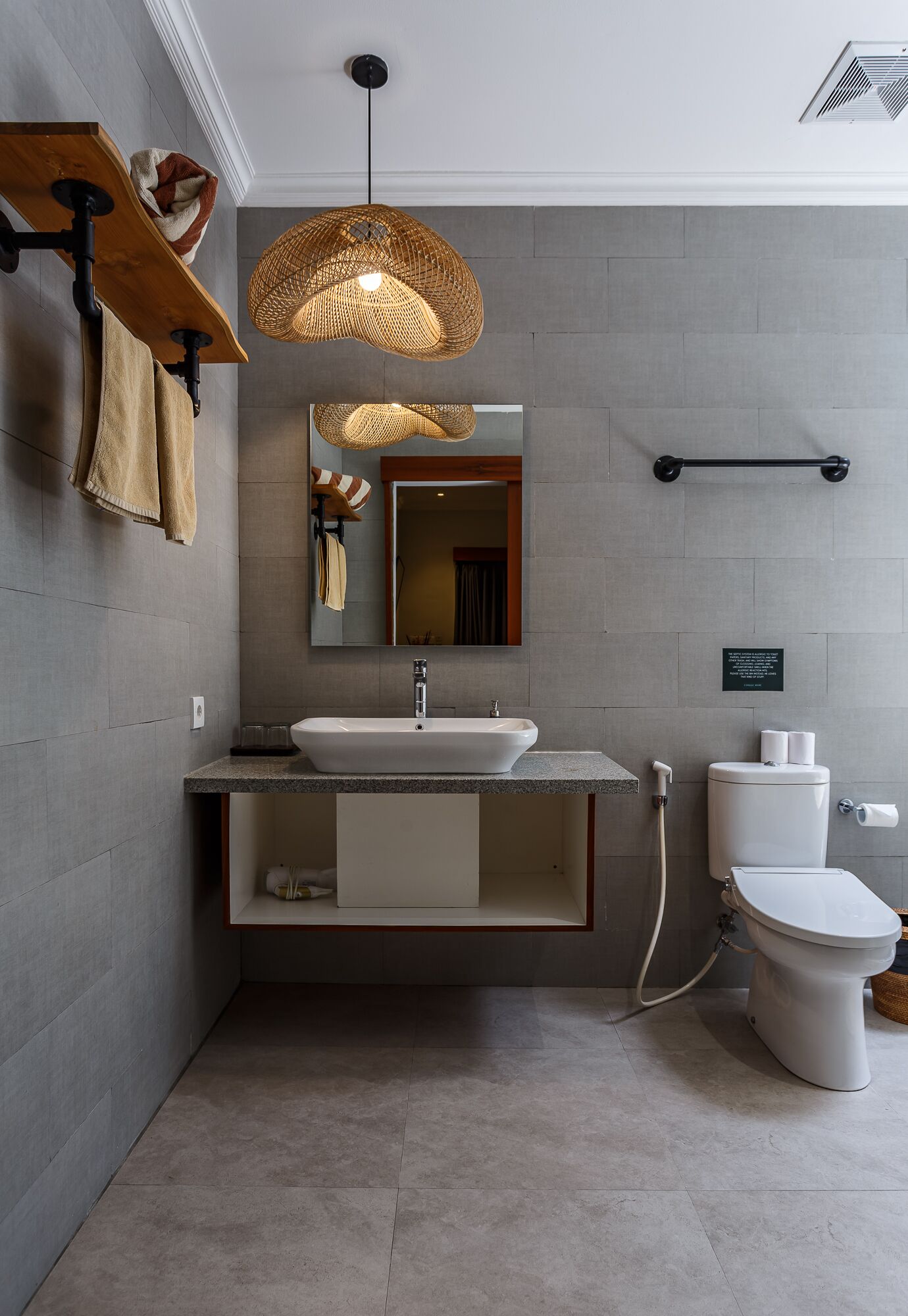 A modern bathroom with a large mirror, a sink, and a toilet. There is a towel rack and a hanging light fixture.