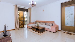 A living room with a sofa, coffee table, TV, and a door with a frosted glass panel. - Kami Luxury Apartment (Kigali)