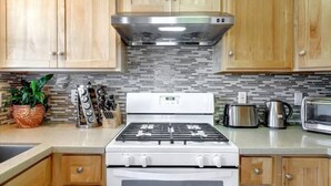 A kitchen with wooden cabinets, a gas stove, a microwave, and a coffee maker. - JadeHome -- Townhome style (Alameda)
