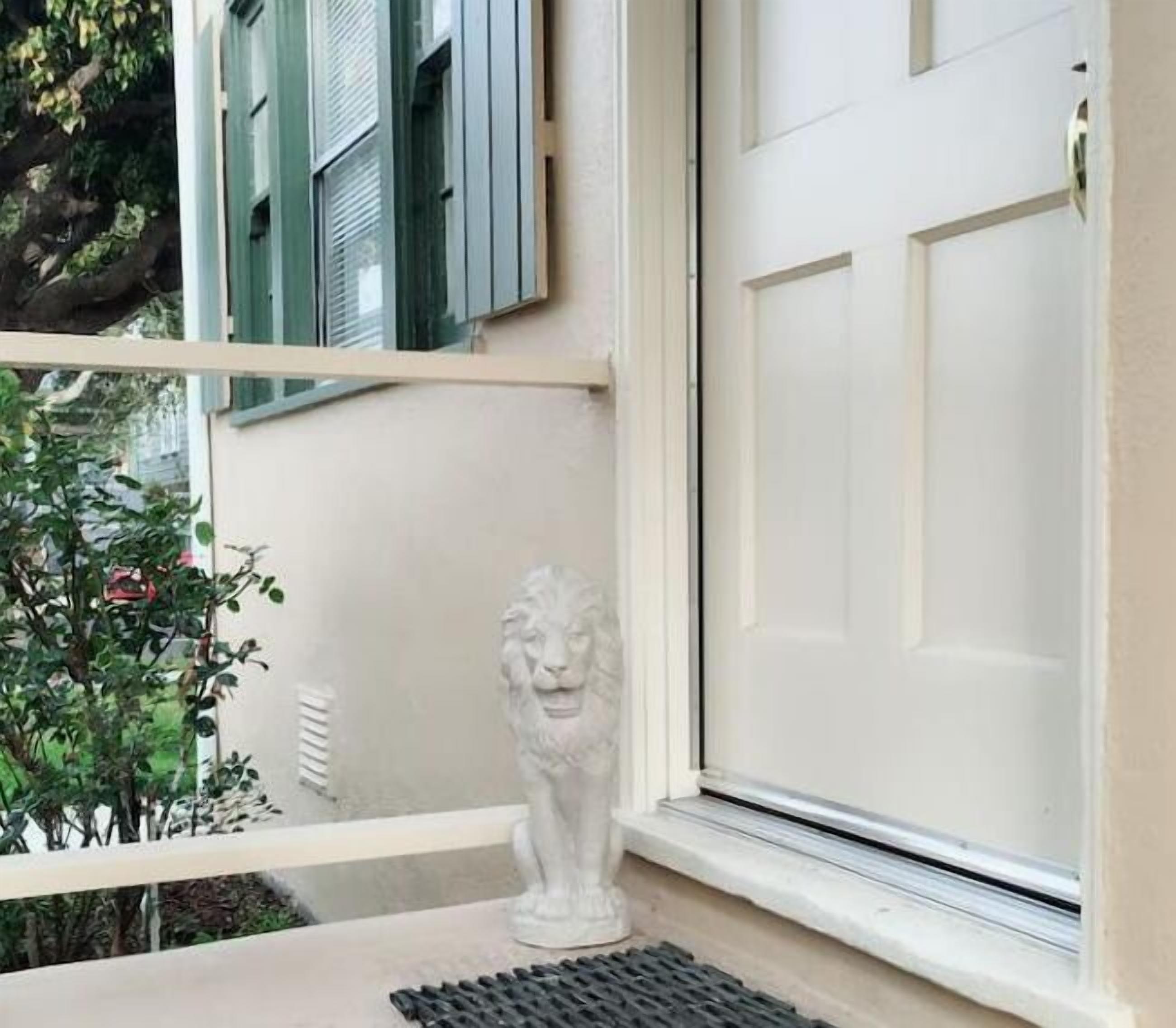 Une fenêtre avec une porte blanche, une statue de lion en pierre sur le rebord de la fenêtre et un balcon doté d’une balustrade.
