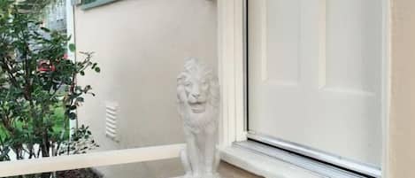 A window with a white door, a stone lion statue on the windowsill, and a balcony with a railing.