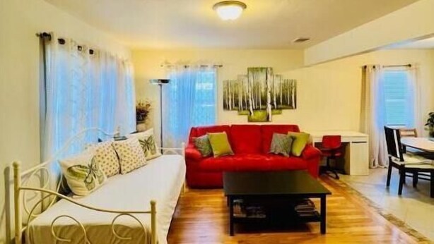 A living room with a bed, a red sofa, a dining table, and a chandelier. - JadeHome -- Townhome style (Alameda)