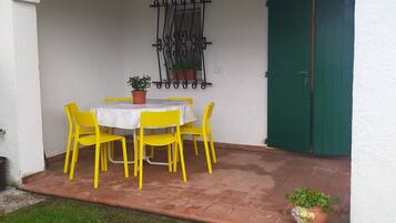 Um pátio com parede branca, porta verde e uma mesa com cadeiras amarelas.