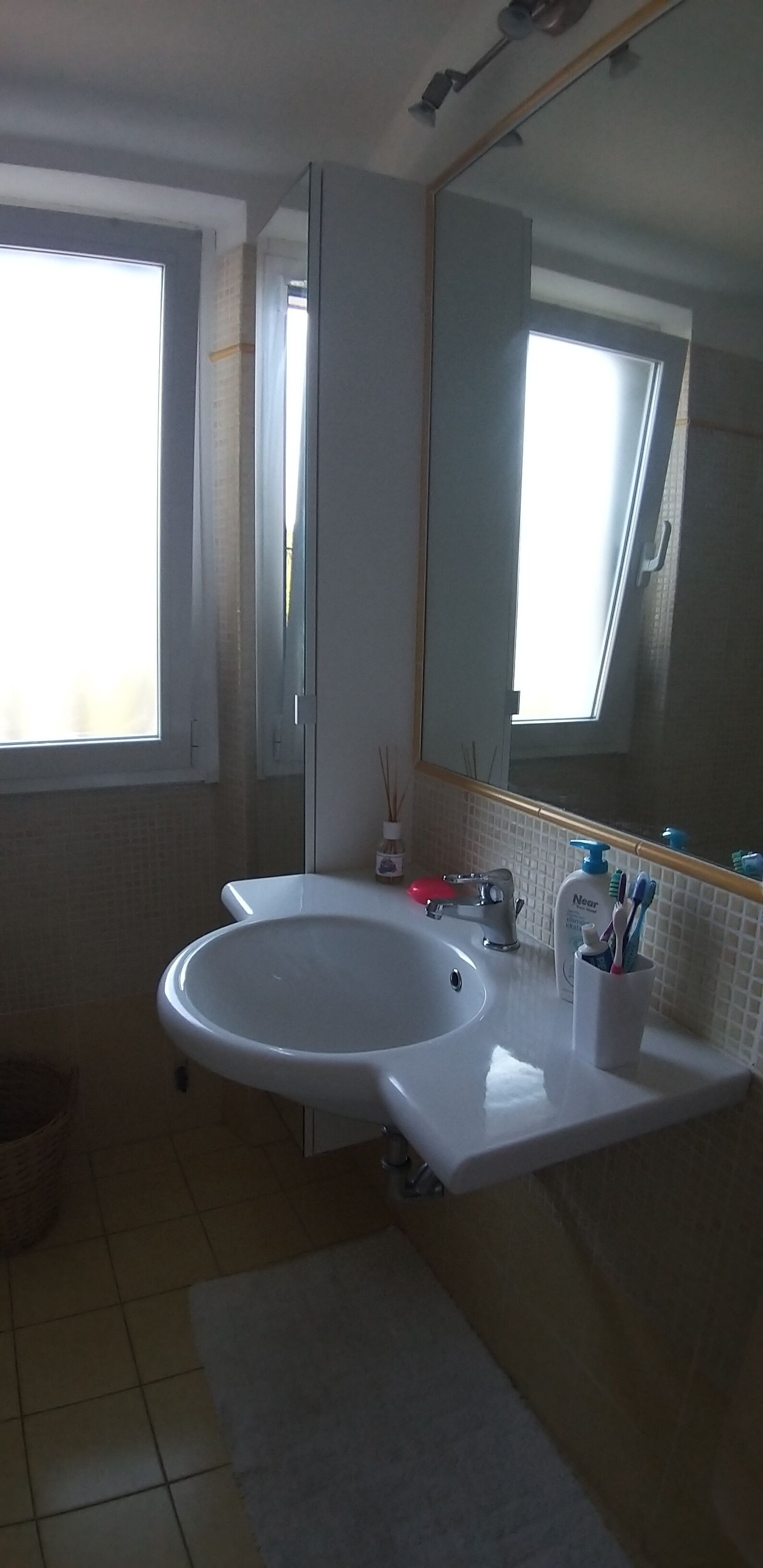 A bathroom with a white sink, a mirror, and a window.