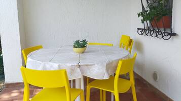 Uma mesa redonda com toalha branca e quatro cadeiras amarelas. Há uma planta em vaso sobre a mesa.
