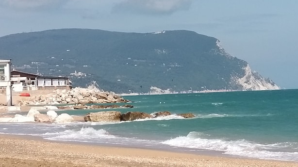 Un paysage côtier avec un bâtiment situé près du rivage, des affleurements rocheux et une montagne en arrière-plan.