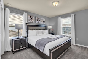 A bedroom with a large bed, a nightstand, a lamp, and artwork on the wall.