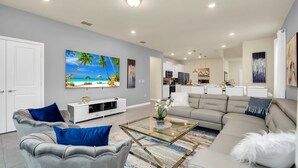 A modern living room with a sectional sofa, a glass coffee table, and a large beach-themed painting on the wall. - Magical Themed Villa in Windsor Isalnd (Davenport)