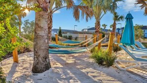A sandy beach area with hammocks and lounge chairs, surrounded by palm trees and a clear sky. - Magical Themed Villa in Windsor Isalnd (Davenport)